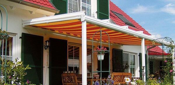Terrasse mit gelb-orange gestreifter Markise an Einfamilienhaus mit Garten und Gartenmöbeln.