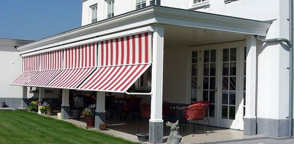 Weiße Terrasse mit rot-weiß gestreifter Markise an modernem Haus im Sonnenschein.
