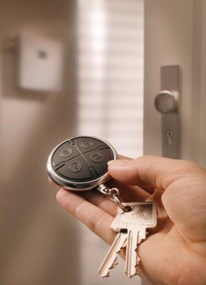 Hand hält Schlüsselbund mit modernem Funkfernbedienung vor einer Wohnungstür.