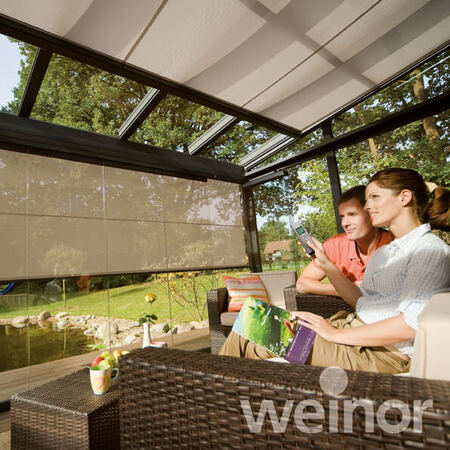 Paar entspannt im modernen Wintergarten mit Glasdach und Sonnenschutz-Markisen.